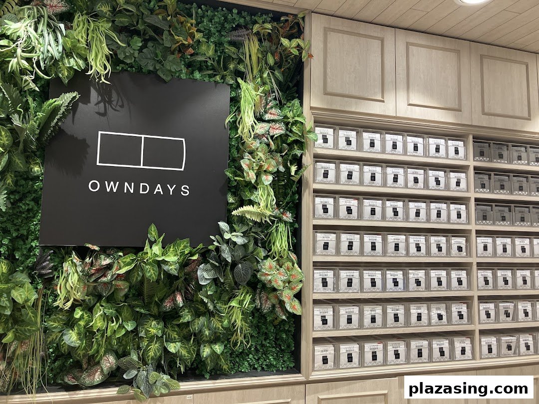The OWNDAYS logo is displayed on a vibrant green wall next to shelves of packaged contact lenses.