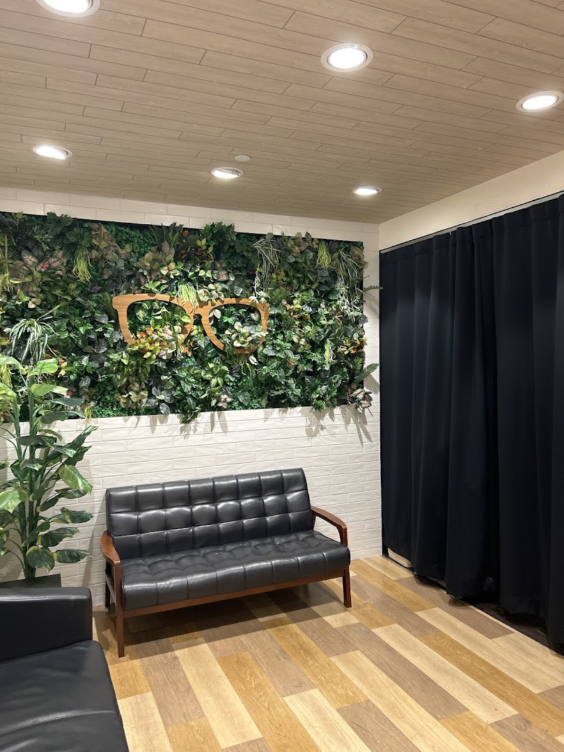 A comfortable waiting area with a black leather sofa, a green wall featuring a large wooden glasses motif, and wooden flooring.