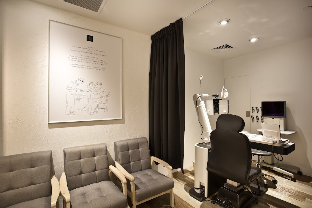 An interior view of an optical shop's eye examination room with waiting chairs and modern equipment.