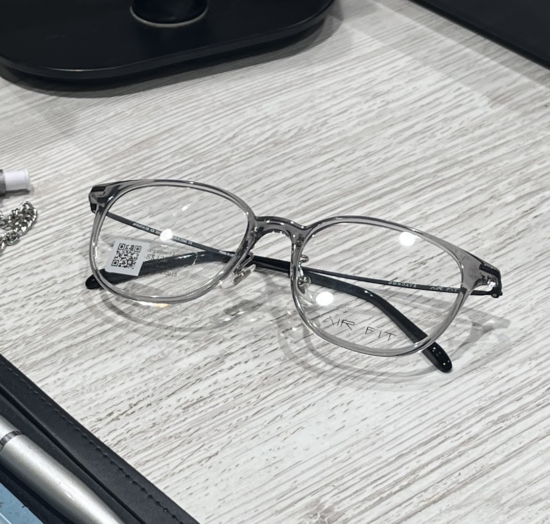 A pair of stylish grey-framed eyeglasses with 'AIR FIT' branding on a light wooden surface.