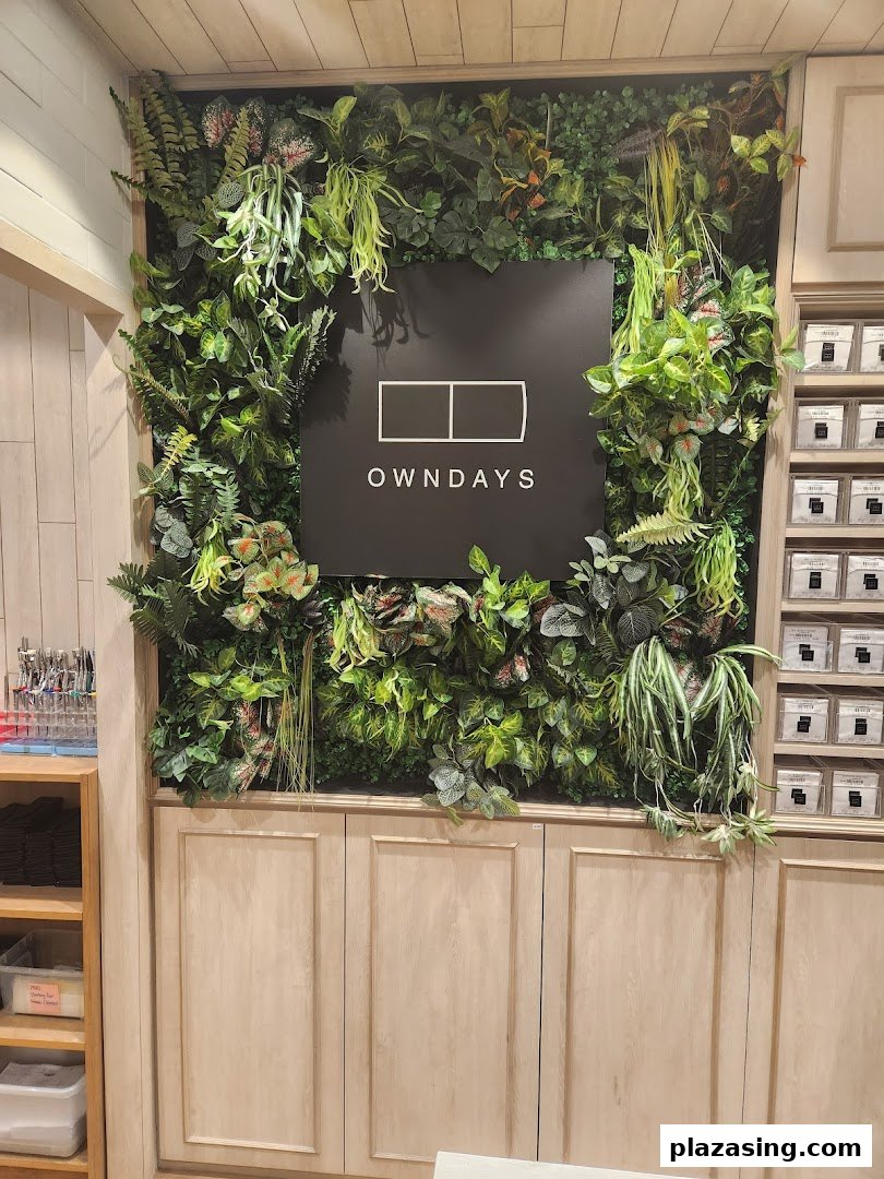 The OWNDAYS logo is prominently displayed on a lush green wall feature inside the store.
