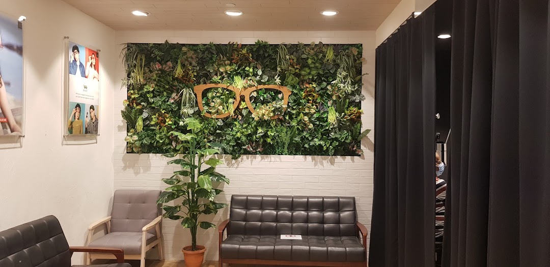 Interior view of OWNDAYS waiting area with green wall art featuring an eyeglasses motif and comfortable seating.