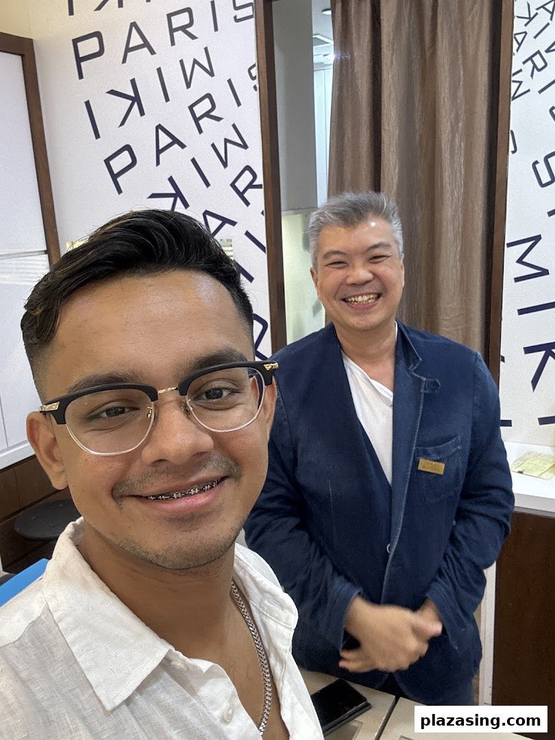 A happy customer wearing new glasses takes a selfie with a smiling staff member at Paris Miki.