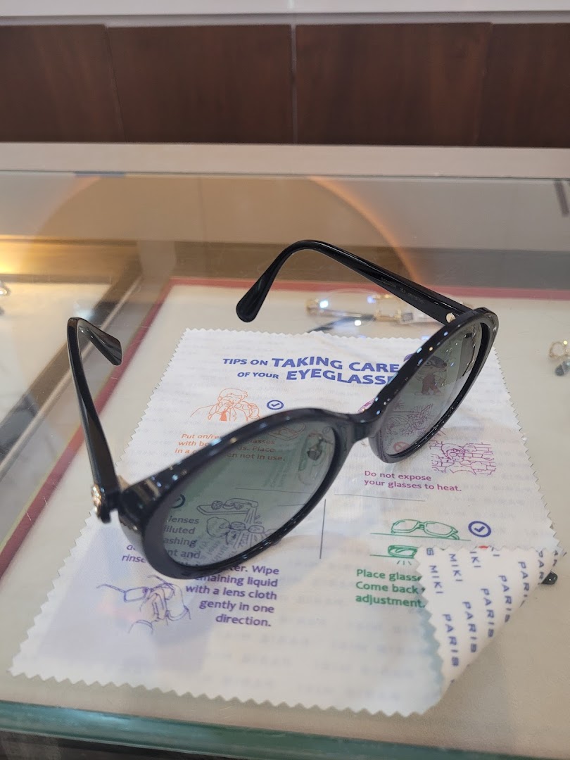 Black sunglasses rest on a Paris Miki branded cleaning cloth with eyeglass care tips.