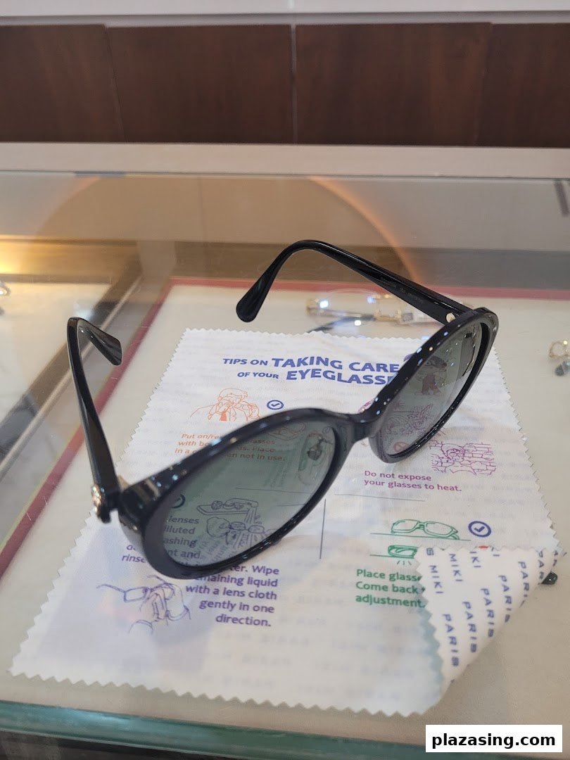 Black sunglasses rest on a Paris Miki branded cleaning cloth with eyeglass care tips.