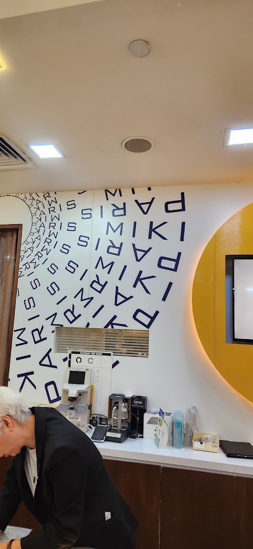 Interior view of Paris Miki optician, showing eye care equipment and a customer at the counter.