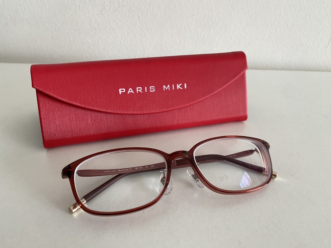 A pair of brown spectacles and a red Paris Miki spectacle case on a white surface.