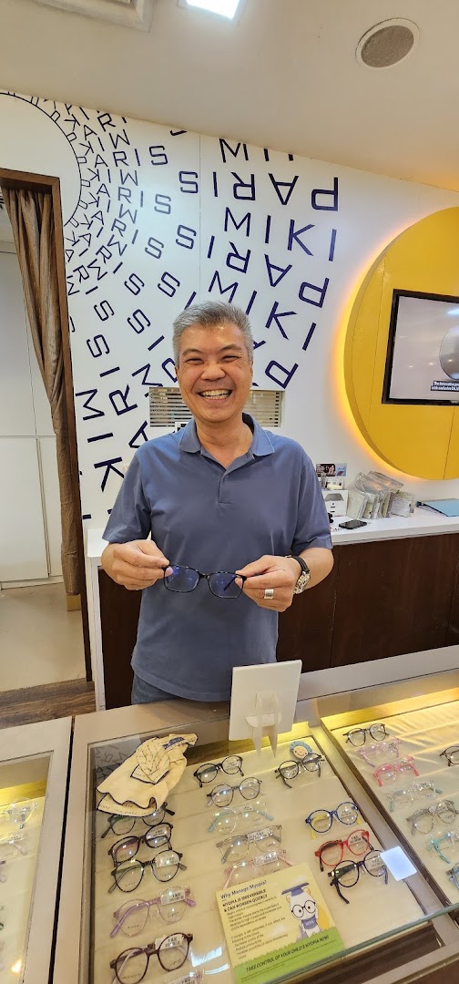 A smiling man holds a pair of glasses in an optical shop, surrounded by eyewear displays.