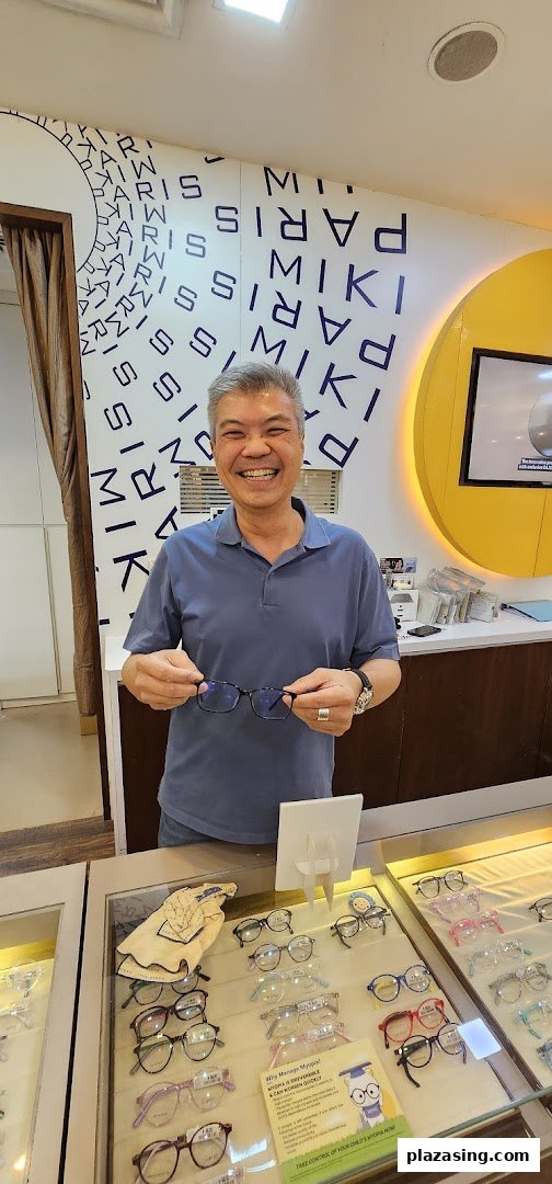 A smiling man holds a pair of glasses in an optical shop, surrounded by eyewear displays.