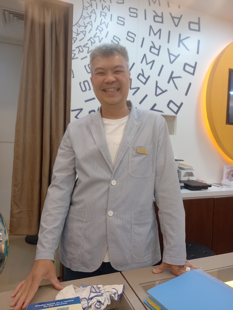 A smiling staff member stands inside Paris Miki optician, ready to assist customers.