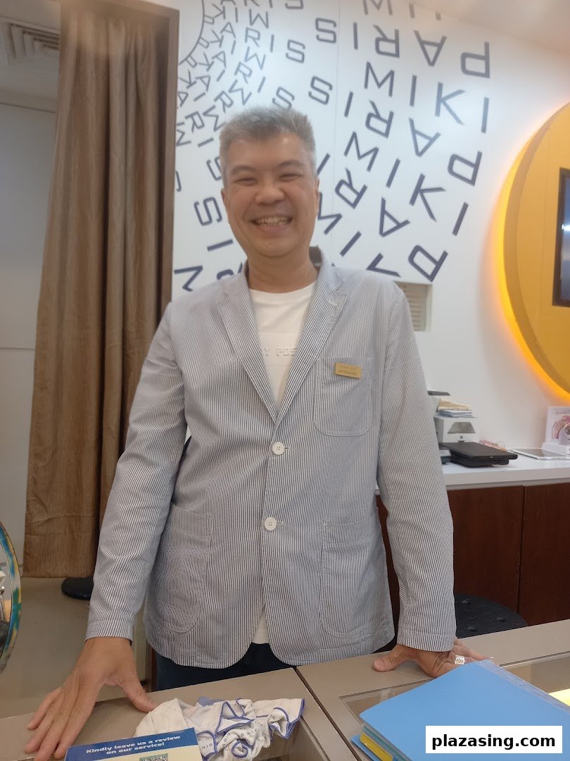 A smiling staff member stands inside Paris Miki optician, ready to assist customers.