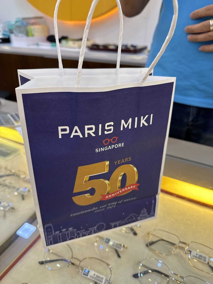 A Paris Miki shopping bag featuring their 50th anniversary design, displayed amidst spectacles.