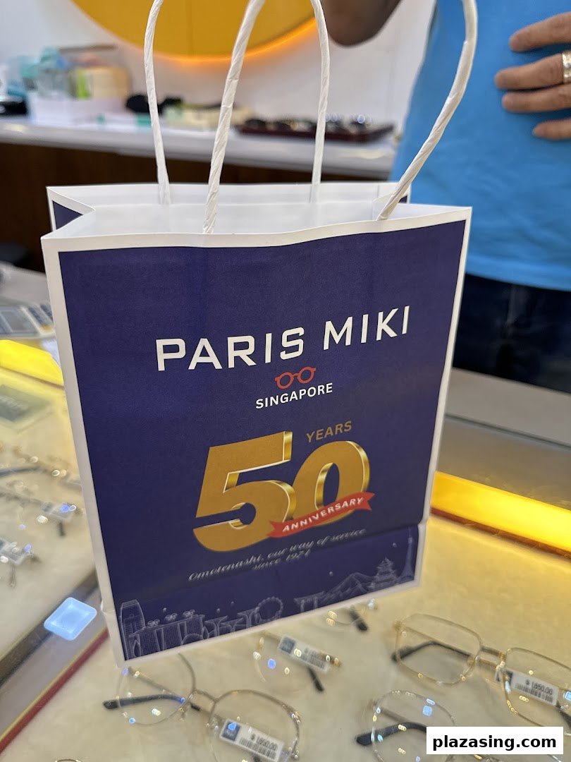 A Paris Miki shopping bag featuring their 50th anniversary design, displayed amidst spectacles.