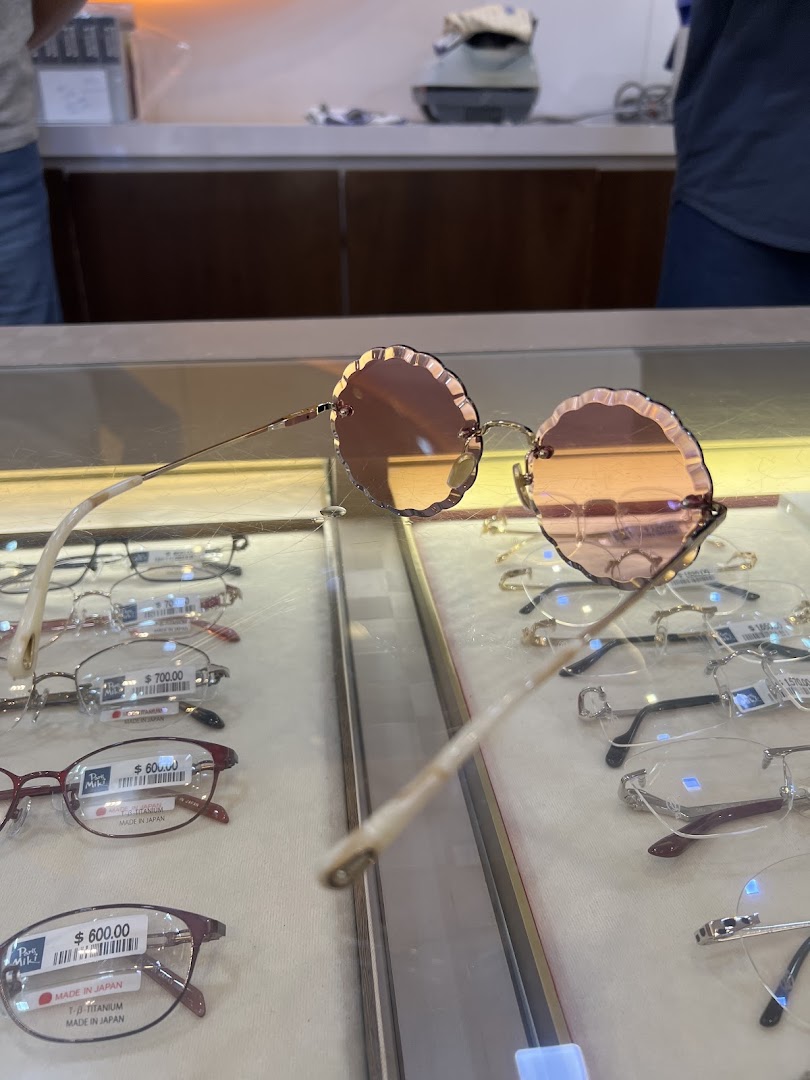 A unique pair of round, scalloped sunglasses displayed on a glass counter with other spectacles.