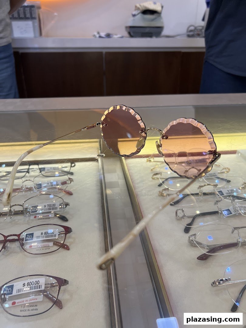 A unique pair of round, scalloped sunglasses displayed on a glass counter with other spectacles.