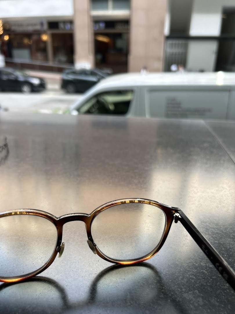 A pair of eyeglasses rests on a surface, with a blurry urban street scene in the background.