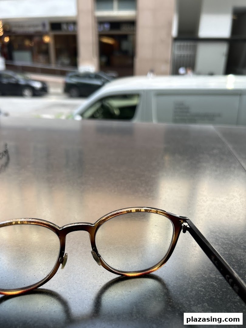 A pair of eyeglasses rests on a surface, with a blurry urban street scene in the background.