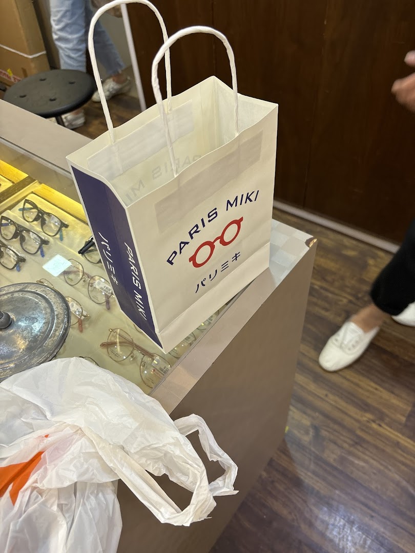 A Paris Miki shopping bag sits on a display counter with eyeglasses visible in the background.