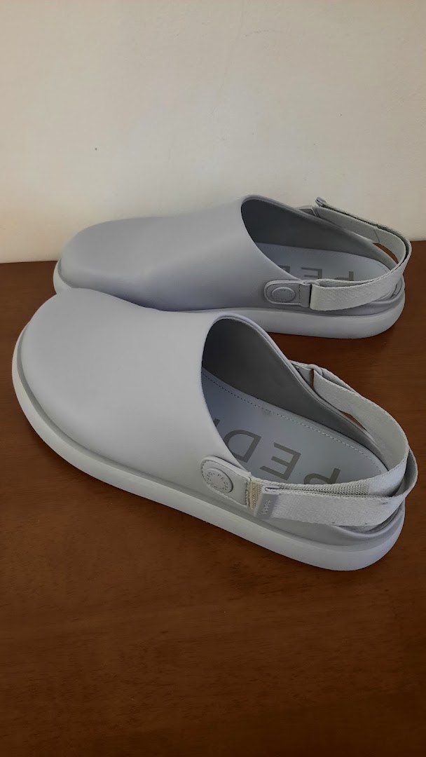 Two light grey, modern clogs with slingback straps are displayed on a wooden surface.