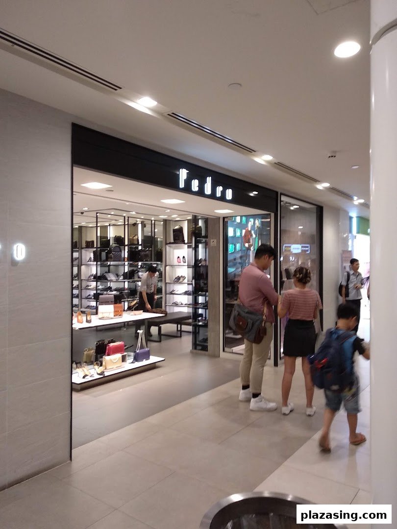 The illuminated entrance of PEDRO at Plaza Singapura, showcasing its modern interior with shoes and bags.