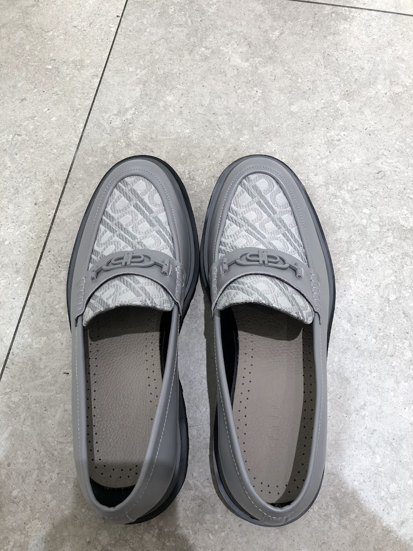 A pair of stylish grey loafers with patterned uppers and metal accents, displayed on a tiled floor.