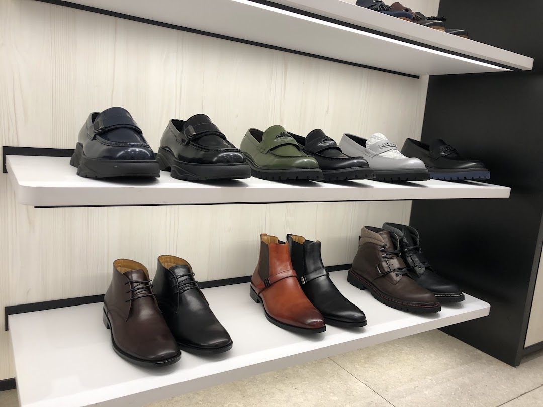 A display of stylish men's shoes and boots on white shelves inside a PEDRO store.