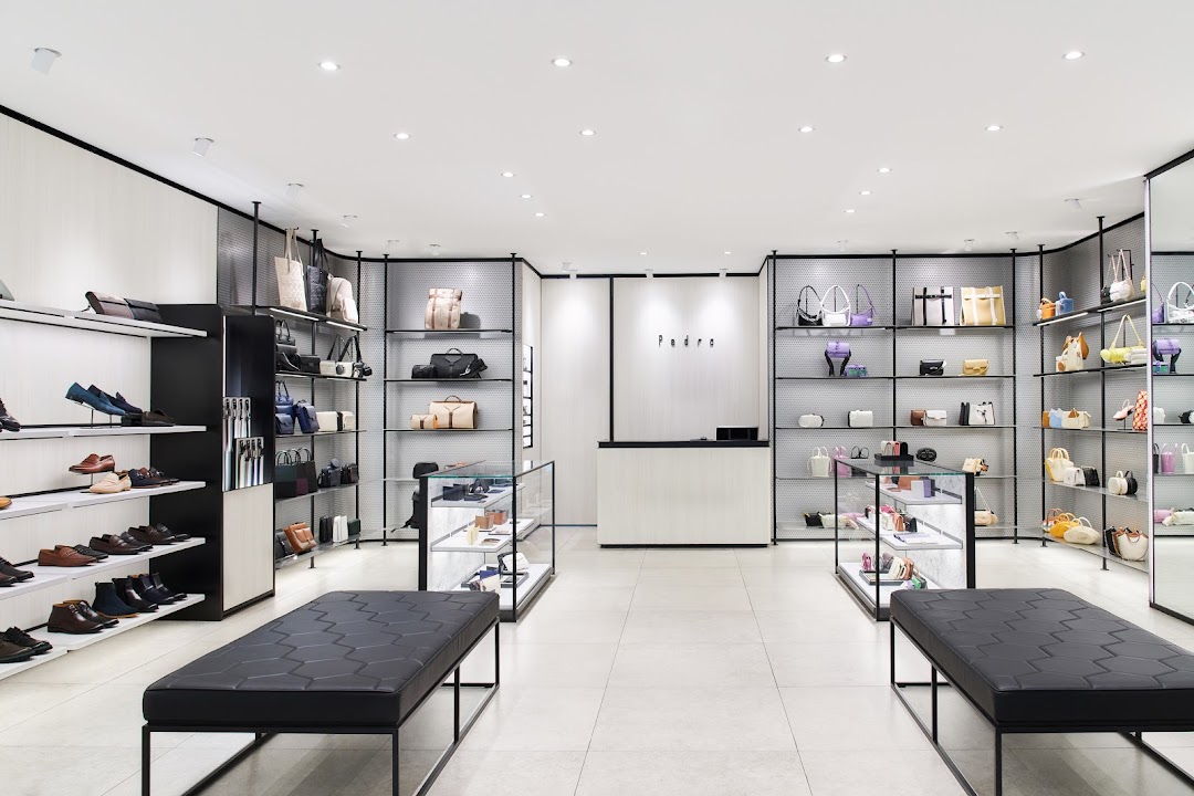A bright, modern retail interior showcasing a wide selection of shoes and handbags on display shelves.