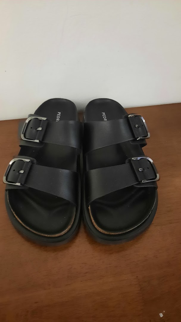 A pair of black Pedro sandals with two buckles displayed on a wooden surface.