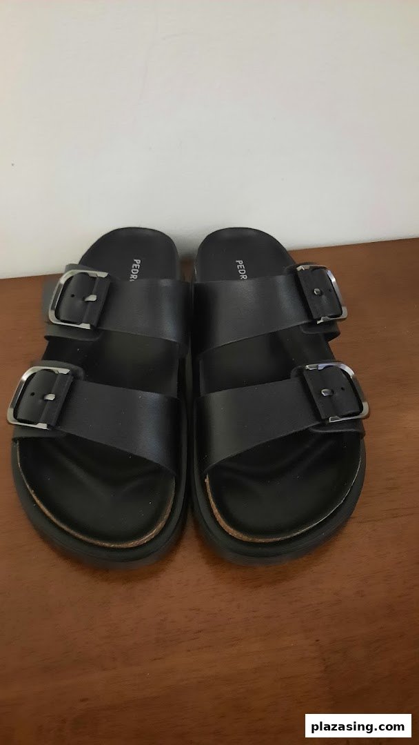A pair of black Pedro sandals with two buckles displayed on a wooden surface.