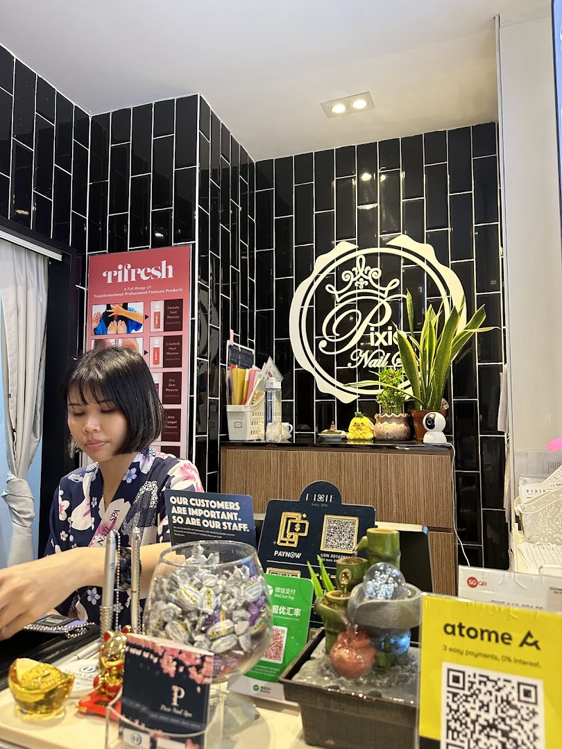 A staff member at the reception counter of Pixie Nail Spa, featuring the shop's logo and various payment options.