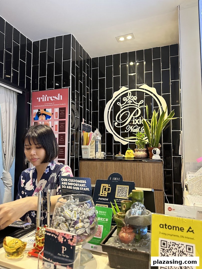 A staff member at the reception counter of Pixie Nail Spa, featuring the shop's logo and various payment options.