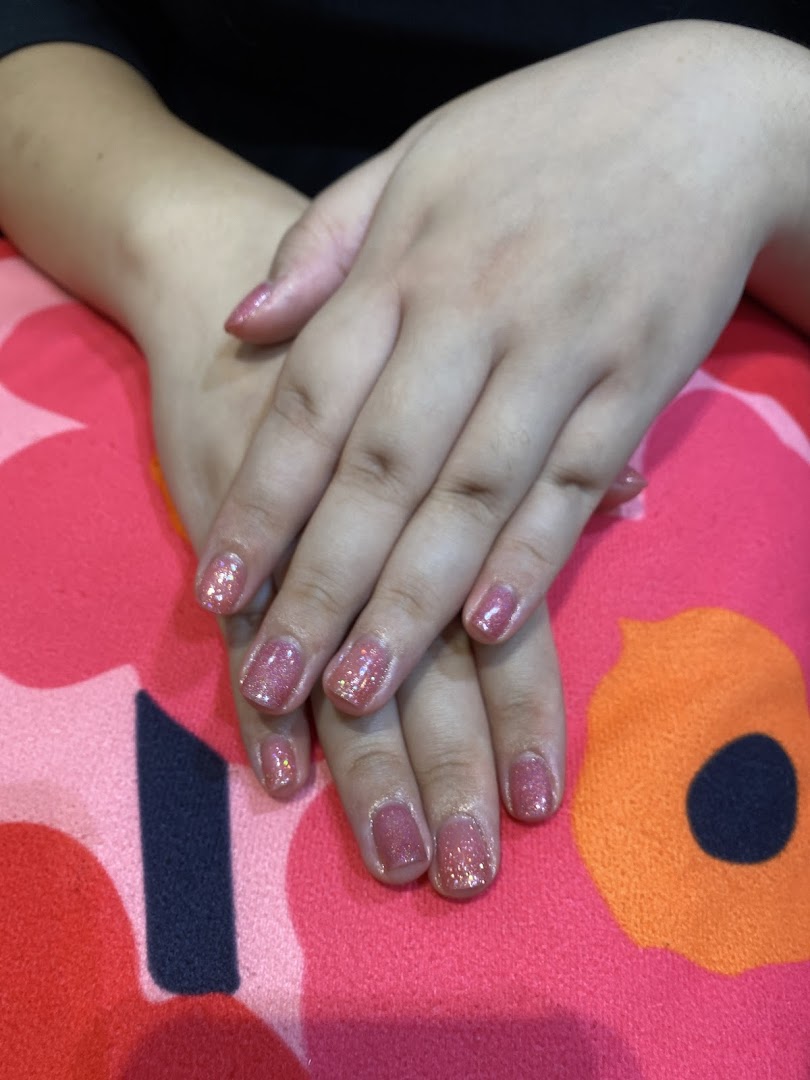 Close-up of hands showcasing a fresh glittery pink nail polish application on a patterned surface.