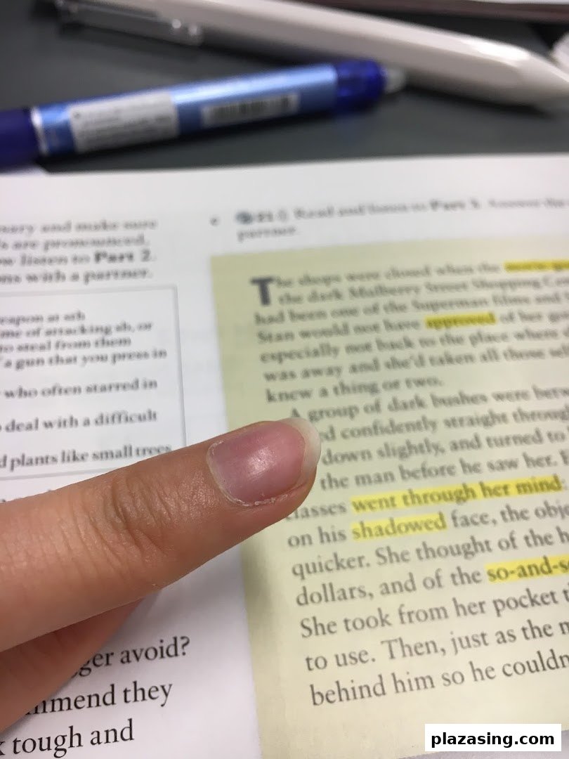 A close-up shot of a finger pointing at highlighted text in an open book, with a pen visible in the background.
