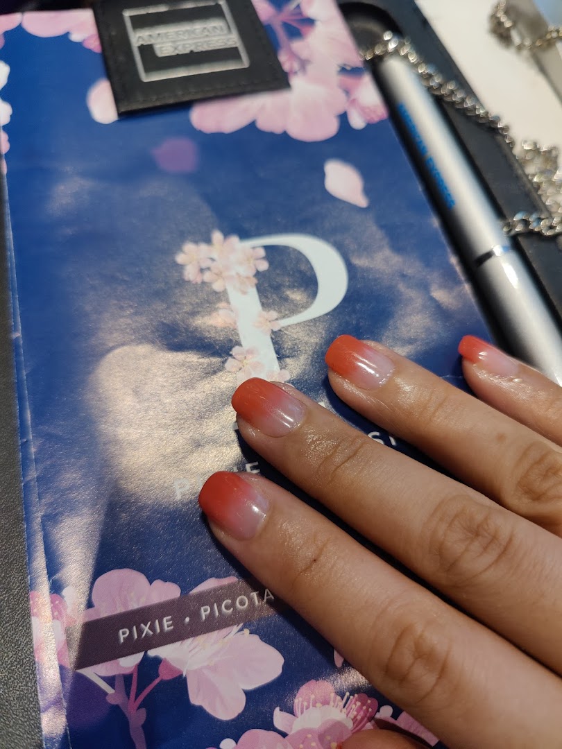 A hand with fresh red ombre nails rests on a cherry blossom-patterned surface, showcasing a beautiful manicure.