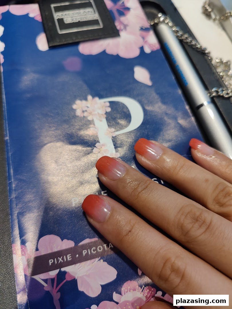 A hand with fresh red ombre nails rests on a cherry blossom-patterned surface, showcasing a beautiful manicure.
