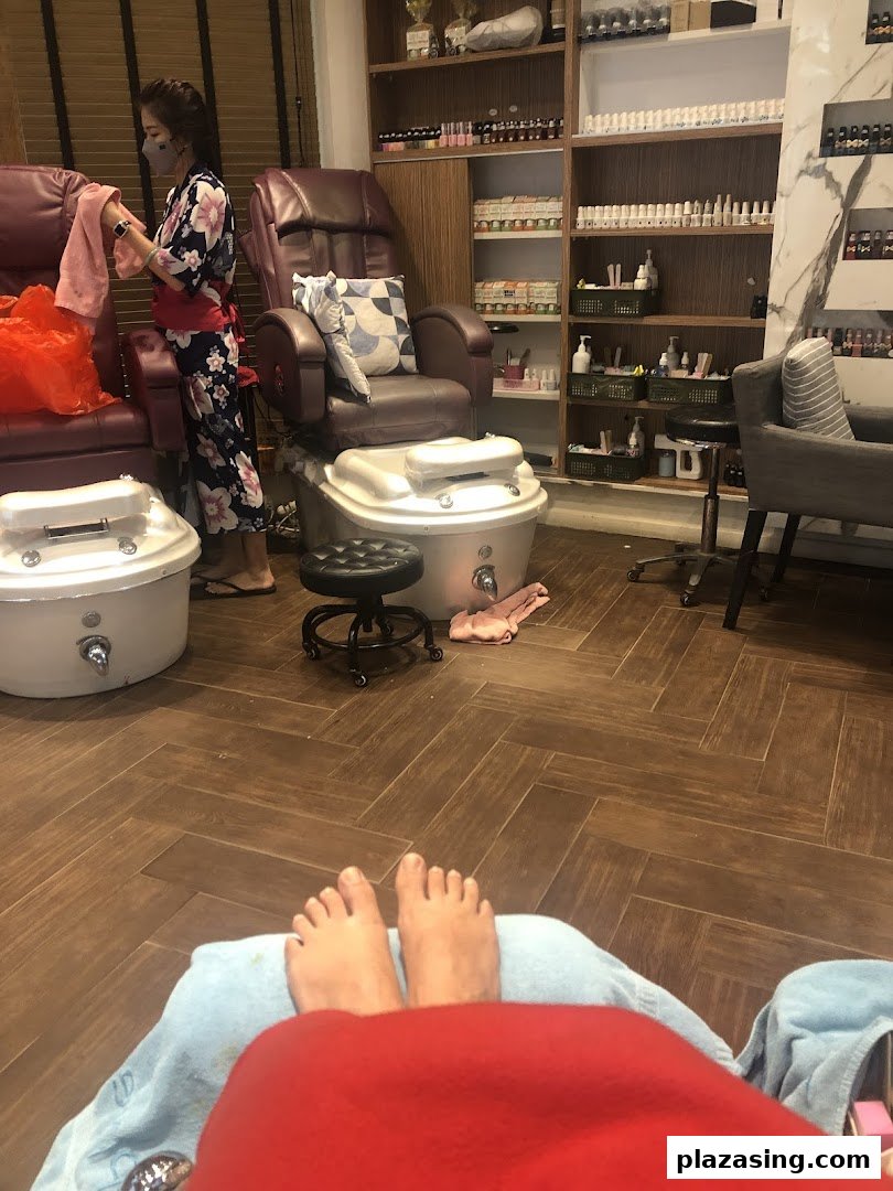 Interior view of a nail spa showing a customer's feet and a staff member attending to a station.
