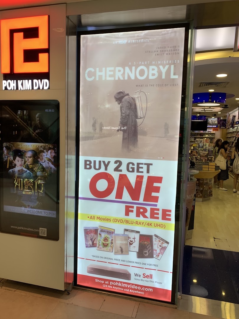 The illuminated storefront of Poh Kim DVD, featuring a large promotional poster for movies and a digital display.
