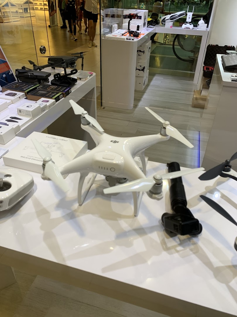 A retail display showcasing various drones, cameras, and tech accessories on white tables.