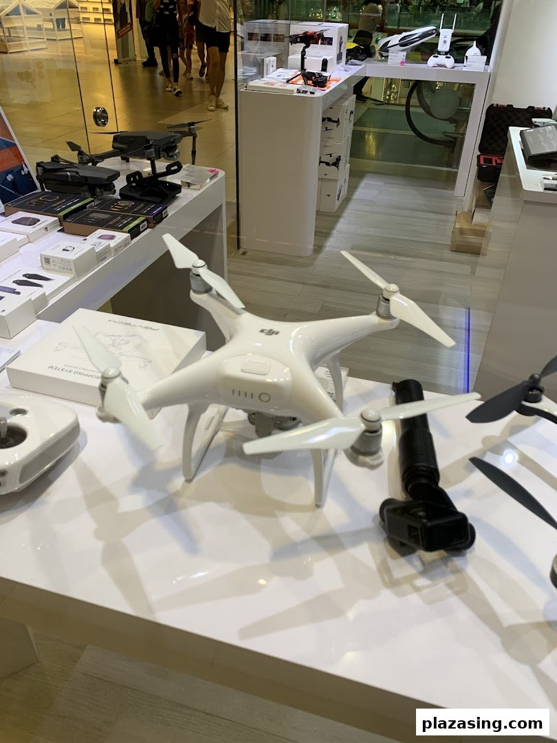 A retail display showcasing various drones, cameras, and tech accessories on white tables.