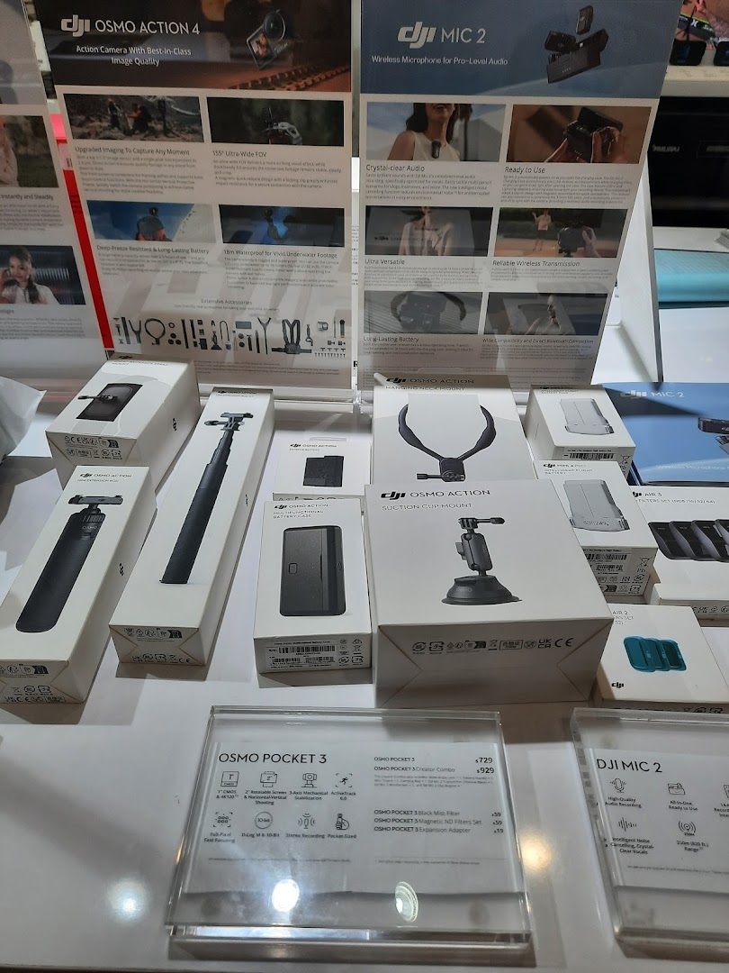 A display of DJI cameras, microphones, and accessories with promotional posters in a retail shop.