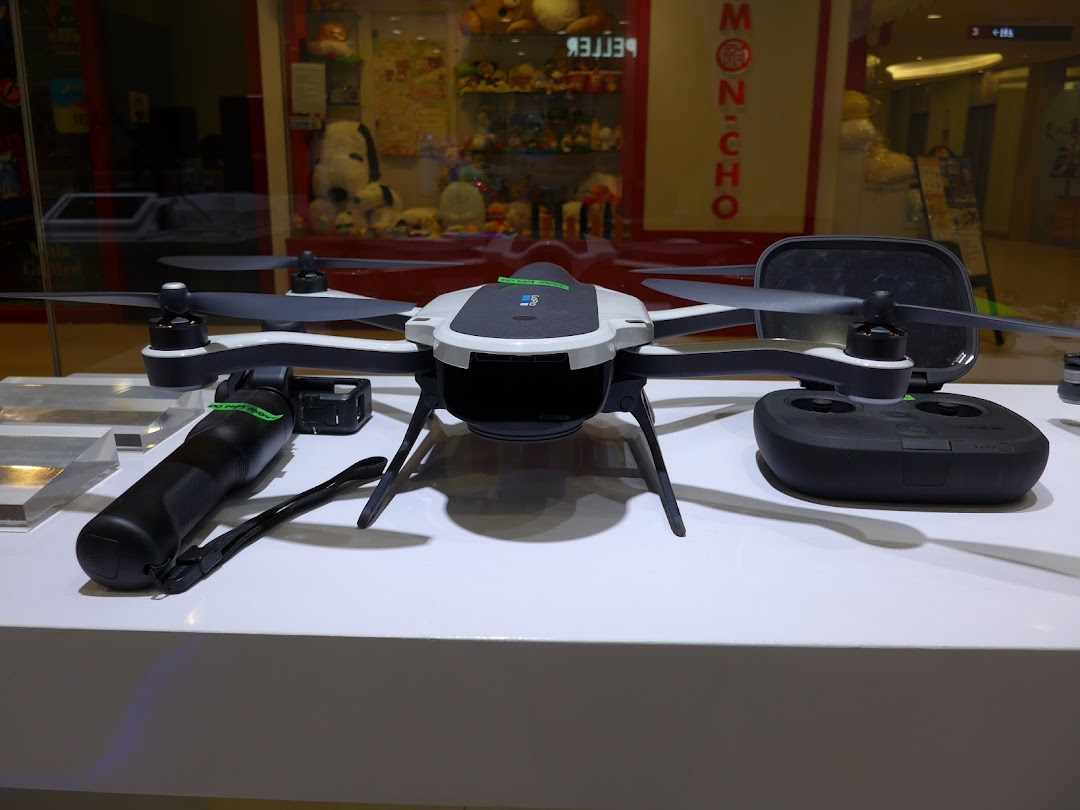 A white and black drone with its remote control and accessories displayed on a white counter.