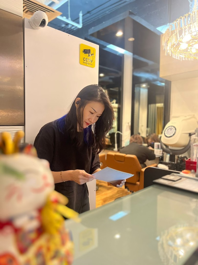 A salon staff member reviews documents at the counter, with a customer visible in the background.
