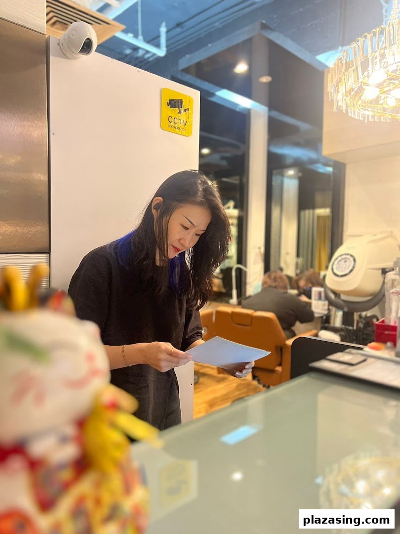 A salon staff member reviews documents at the counter, with a customer visible in the background.