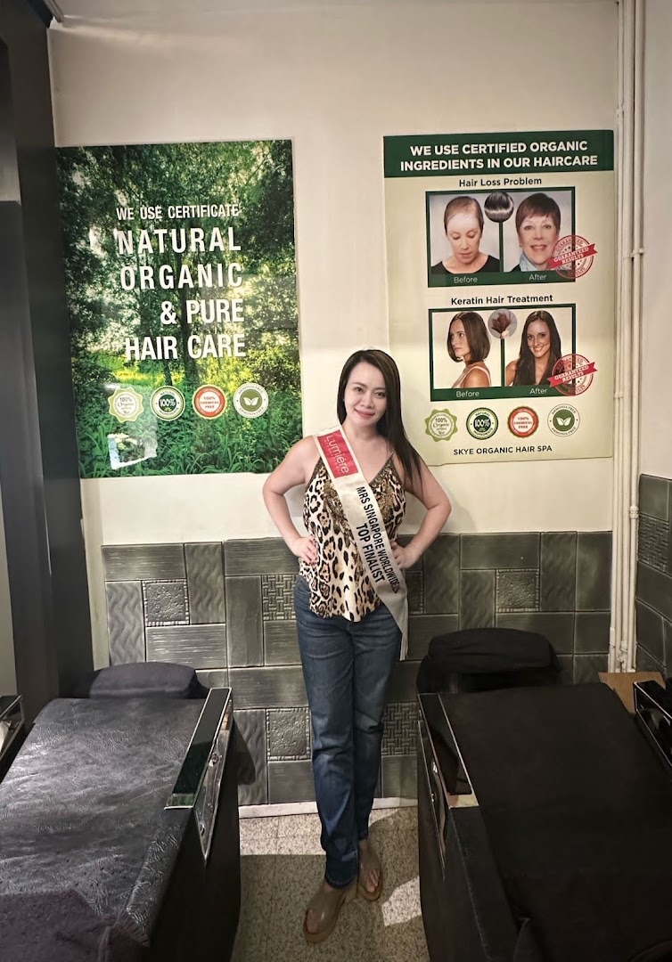 A woman stands in a salon interior featuring posters for natural, organic hair care and treatments.