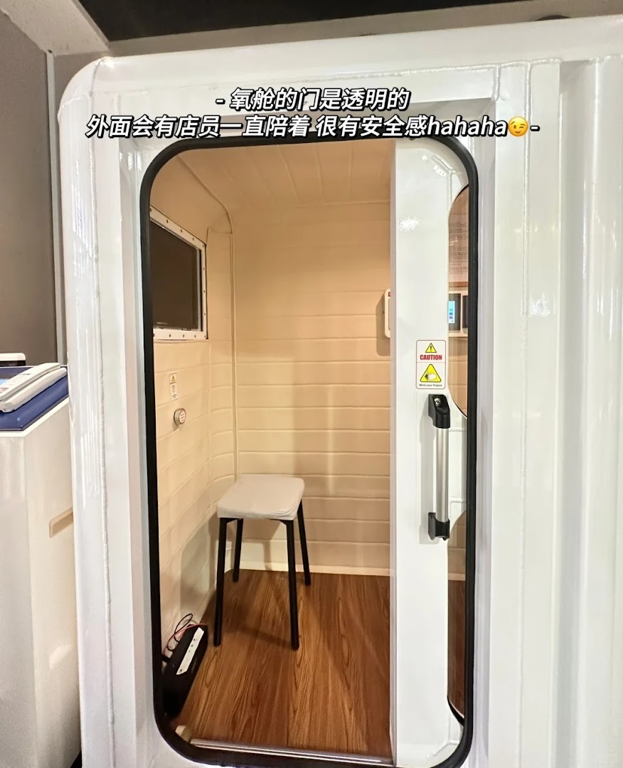 Interior view of a modern white wellness pod, likely an oxygen chamber, with a stool inside.