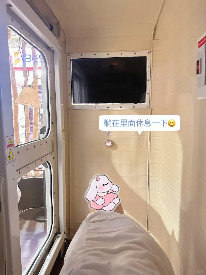 A person relaxing inside a modern wellness pod with a screen and window.
