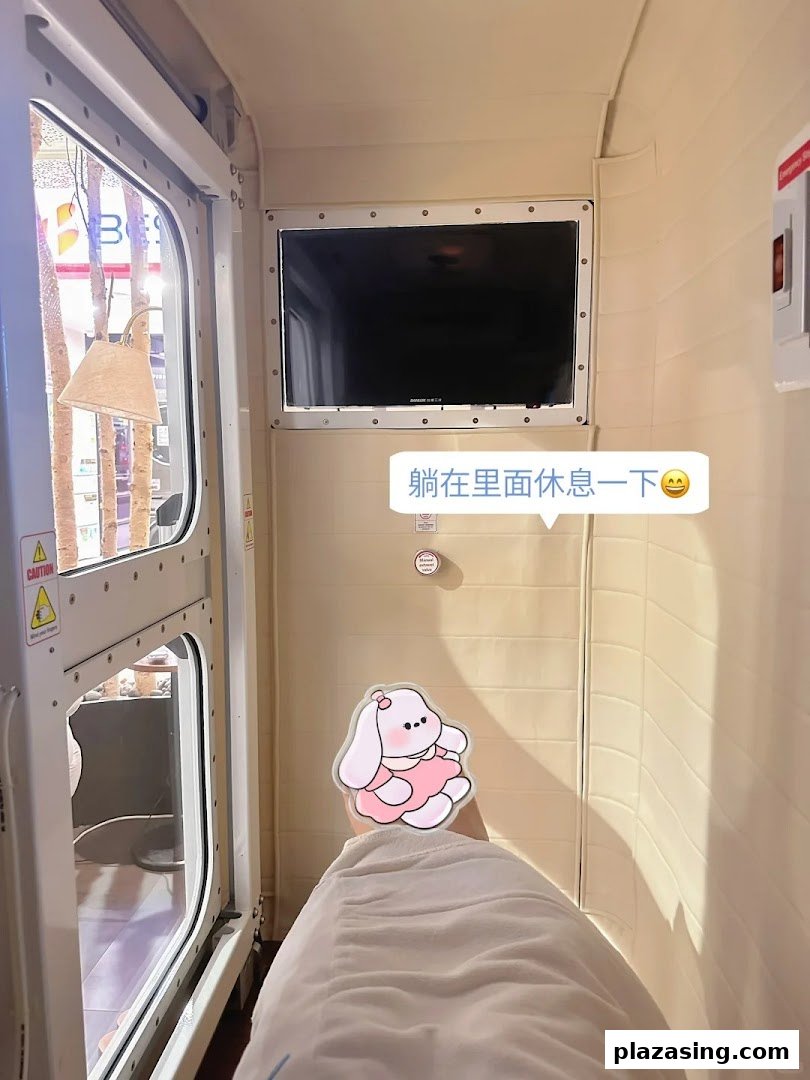 A person relaxing inside a modern wellness pod with a screen and window.