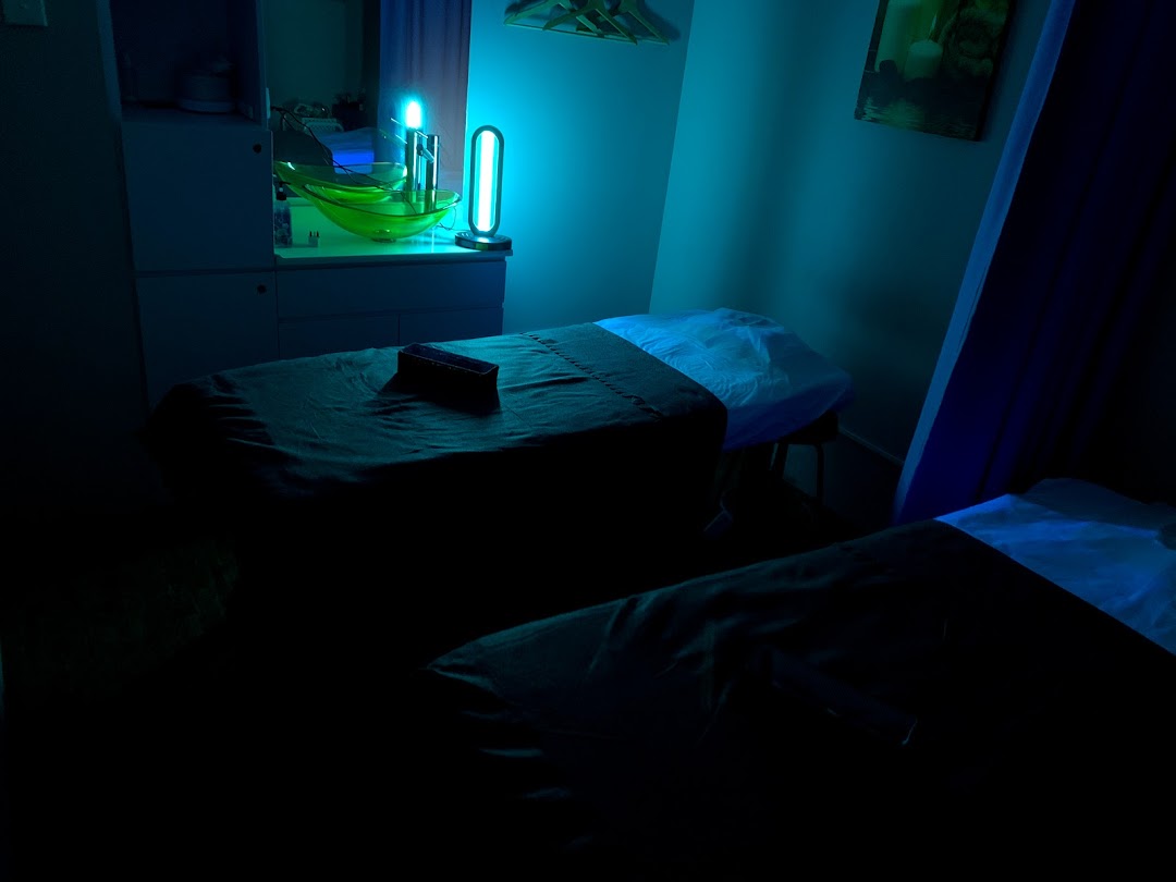 A dimly lit, tranquil treatment room with two massage beds and a blue light fixture.