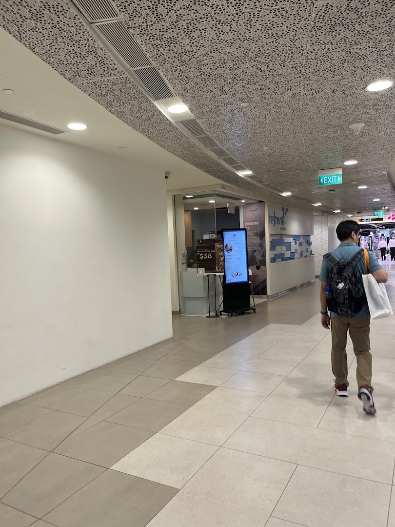A person walks past the inviting entrance of Refresh TCM Wellness in a modern shopping mall.
