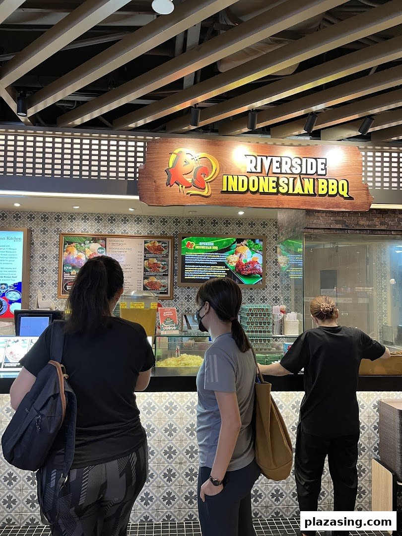 Customers queue at Riverside Indonesian BBQ counter, featuring vibrant menu displays and a welcoming atmosphere.